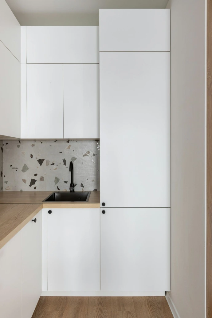 Modern white kitchen with wooden countertop and terrazzo backsplash.